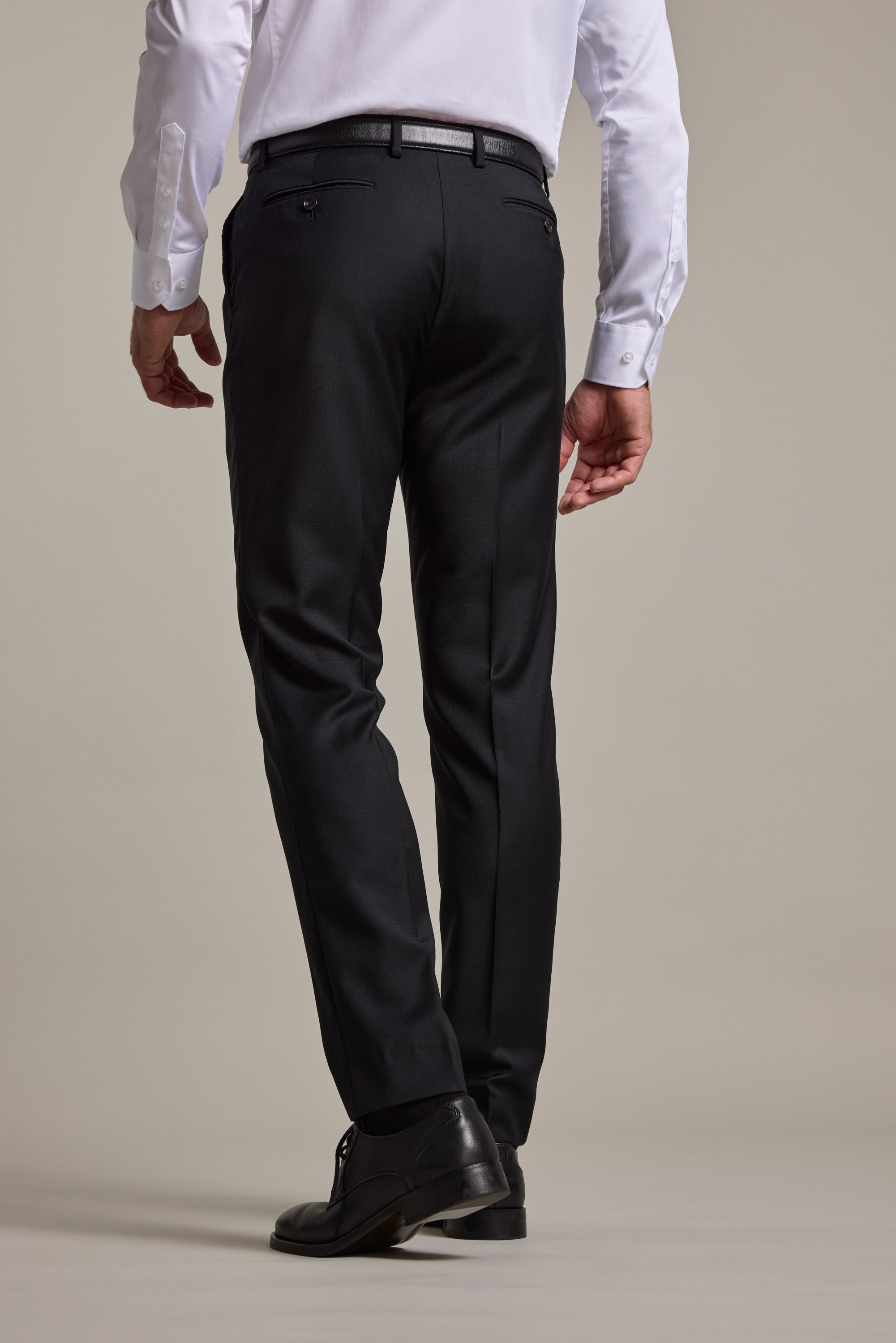 A man wearing a white dress shirt, Barkers Mayfair ZQrx Suit Trouser, and black shoes stands with his back to the camera against a plain light background.