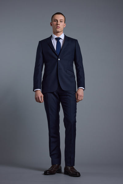 Man wearing Barkers Mayfair ZQrx Suit Trouser in dark blue stands against a gray background.