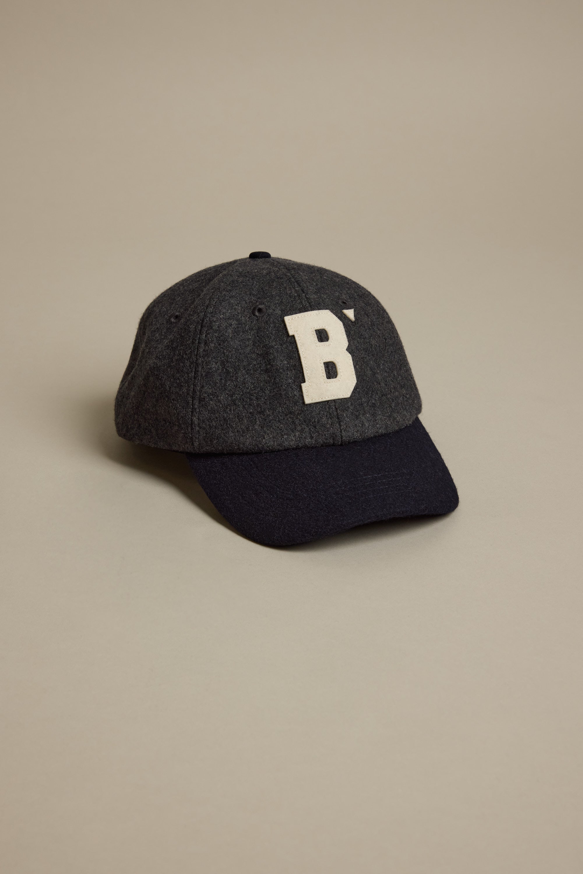 The Darcy Woollen Cap by Barkers, in dark gray wool with a black bill and a bold white 'B' patch logo on the front, is shown against a plain light beige background.
