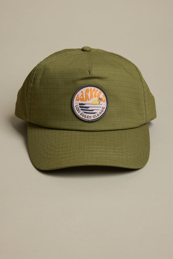 The Barkers Longboard Cap in olive green features an adjustable snapback and a round embroidered patch with "BARKERS" and a stylized sunset on the front, shown against a plain beige background.