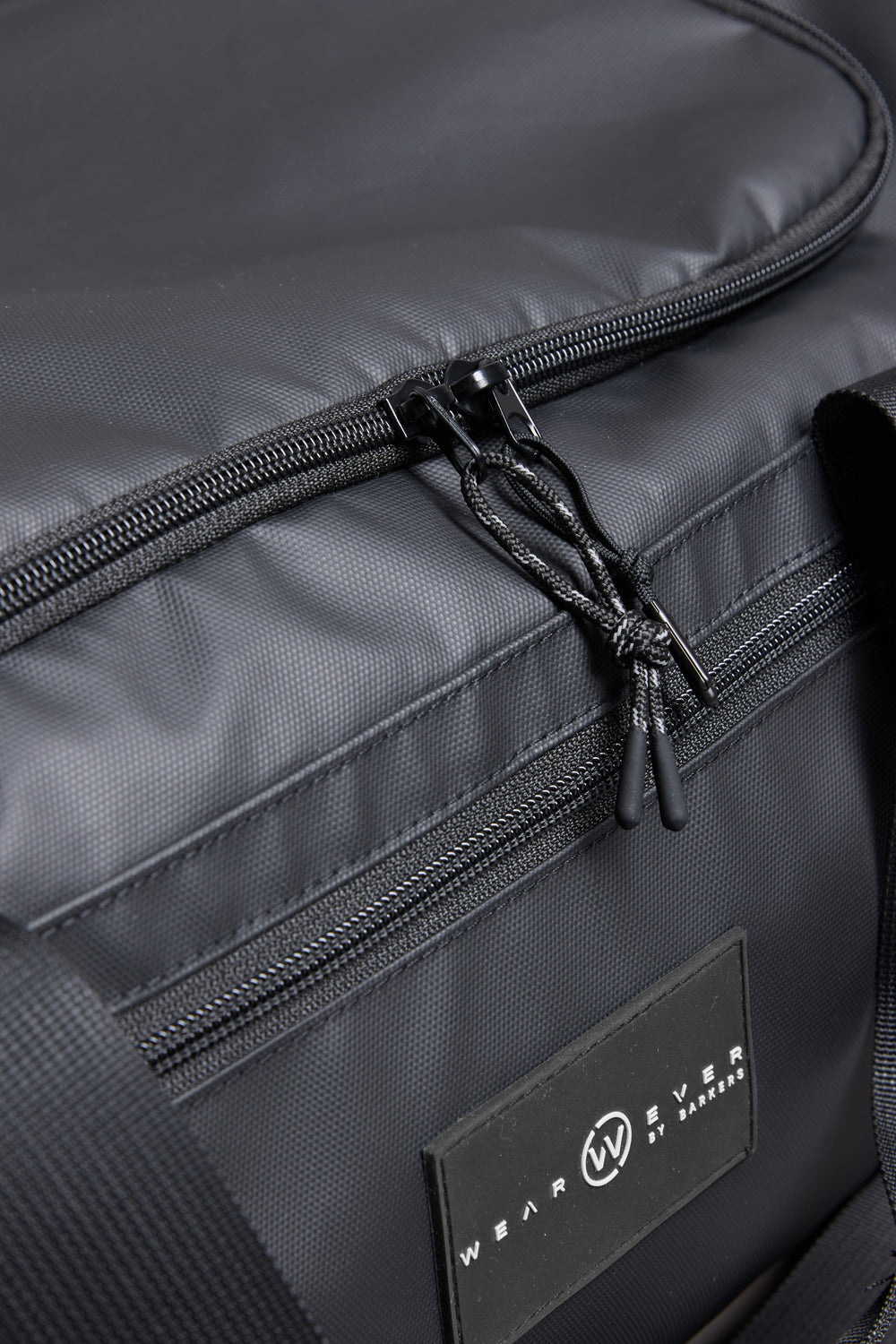 Close-up of the WearEver Transit Holdall, a black duffel bag with visible zipper pulls and a WearEver label. Made from textured, water-resistant fabric, it offers detailed stitching and versatile storage for travel essentials.