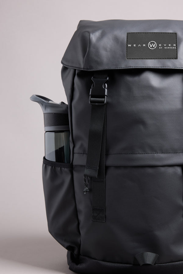 The WearEver Transit Backpack in black features a front buckle, a signature WearEver patch on the flap, water-resistant zips, and a padded laptop sleeve. A water bottle fits into the side pocket. Shown on a plain light gray background.