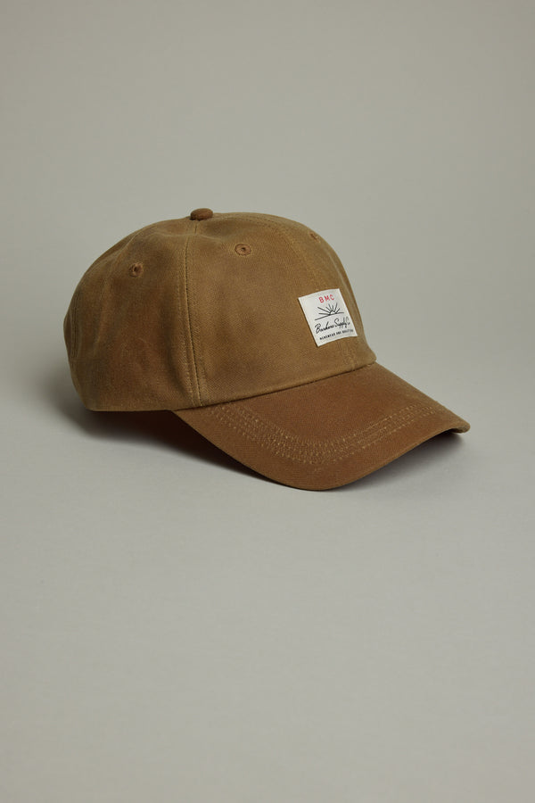 The Barkers Benson Waxed Cotton Cap features brown waxed cotton, a curved brim, and a white rectangular front patch. It offers an adjustable fit and is shown against a plain light gray background.