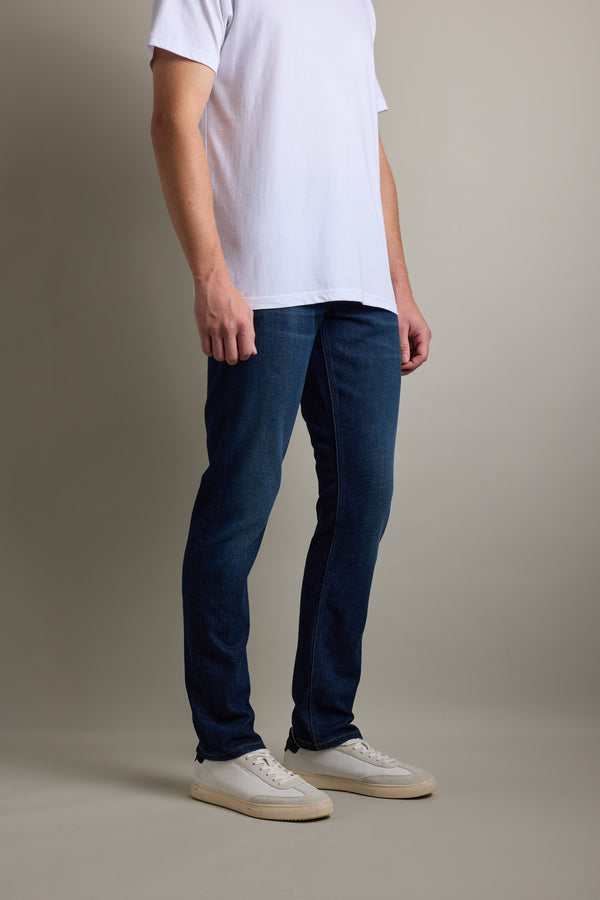 Person in a white tee, Barkers Nomad Denim Taper Jean, and white sneakers stands by a plain background.