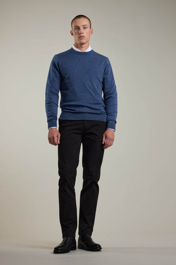 A person stands facing forward against a plain light background, wearing a Barkers Skyland ZQrx Merino Crew sweater made from ethically sourced New Zealand merino wool, over a white collared shirt, black pants, and black shoes.