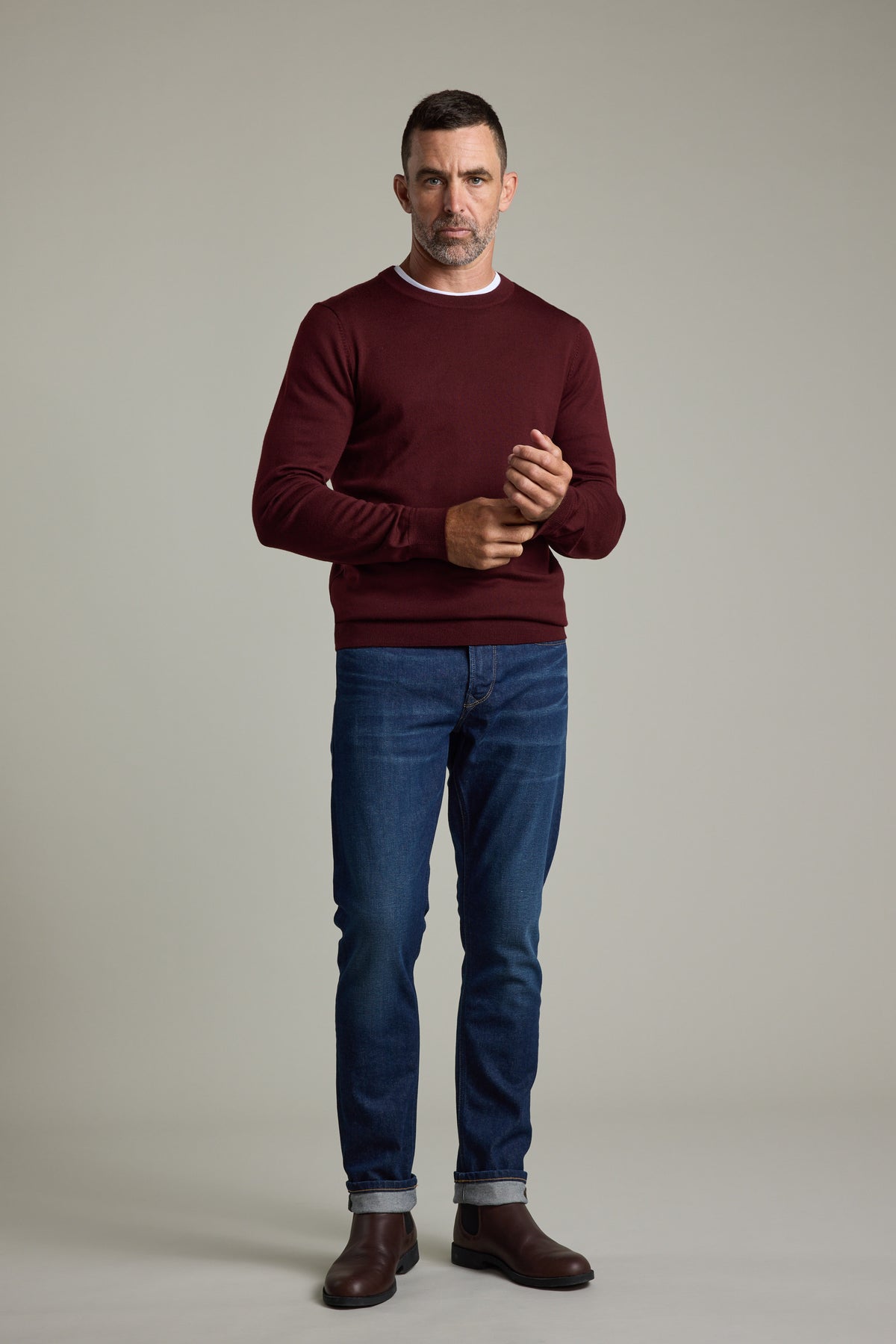Man in a Barkers Skyland ZQrx Merino Crew, blue jeans, and brown boots against a plain background.