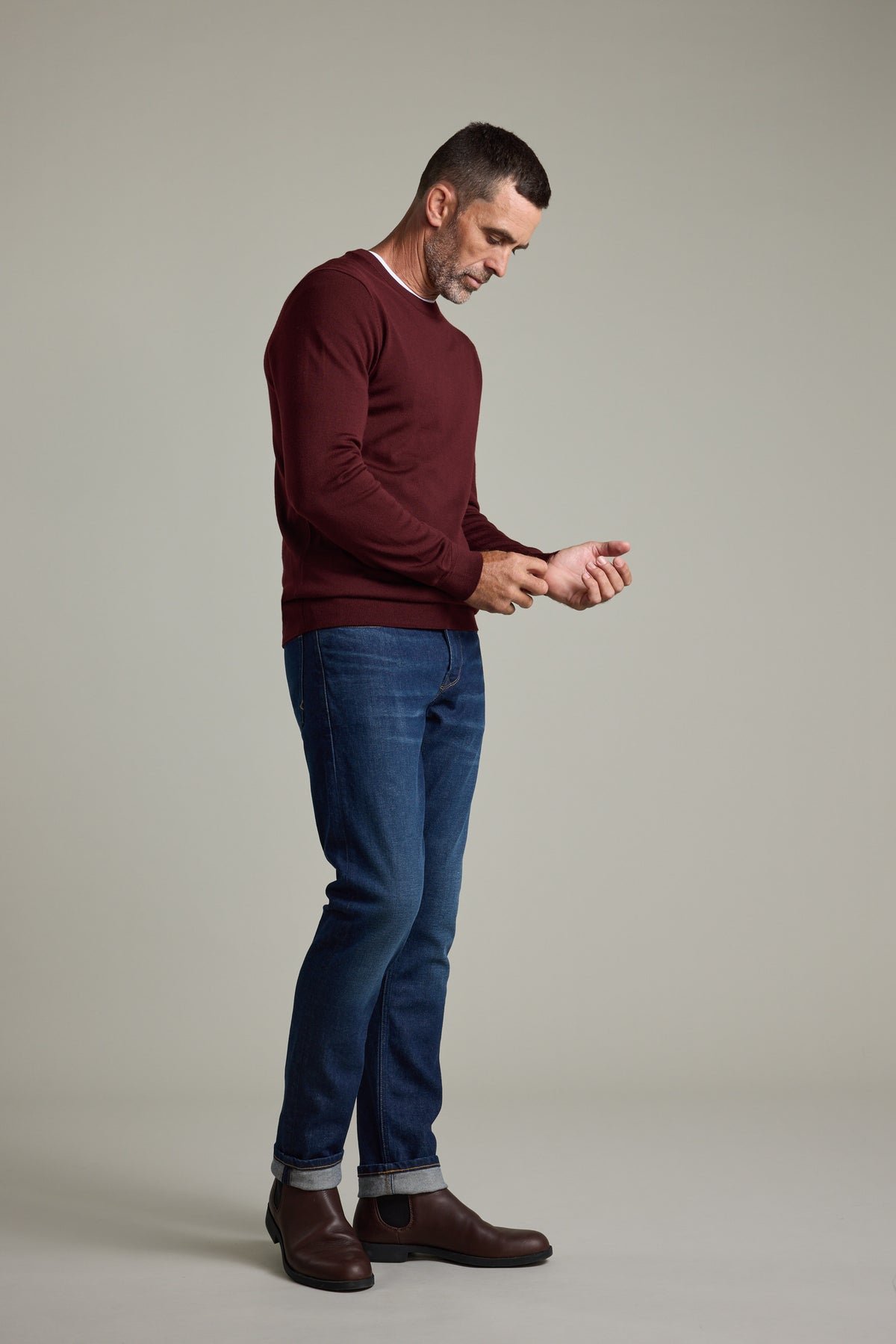 Man in a Barkers Skyland ZQrx Merino Crew and jeans looks down, adjusting his sleeve.