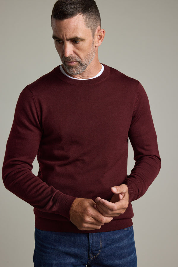 Man in a Barkers Skyland ZQrx Merino Crew and jeans stands against a plain background, looking down.