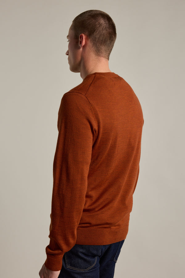 A person with short hair, wearing a rust Skyland ZQrx Merino Crew by Barkers and dark jeans, stands facing away from the camera against a neutral background.