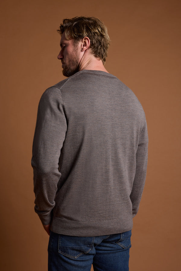 A man with light hair, dressed in a Barkers Skyland ZQrx Merino Crew and blue jeans, stands facing away against a plain brown background.