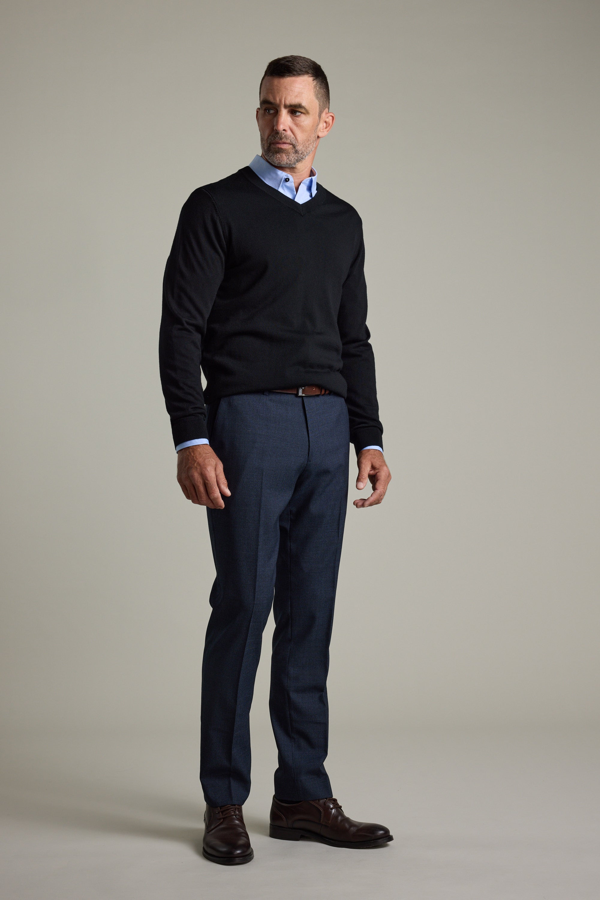 Man wearing Barkers Skyland ZQrx Merino Vee, blue shirt, dress pants, and brown shoes indoors.
