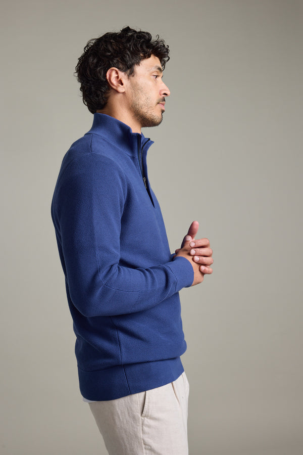 Man in Barkers Gaston Cotton 1/4 Zip Sweater and beige pants stands sideways.