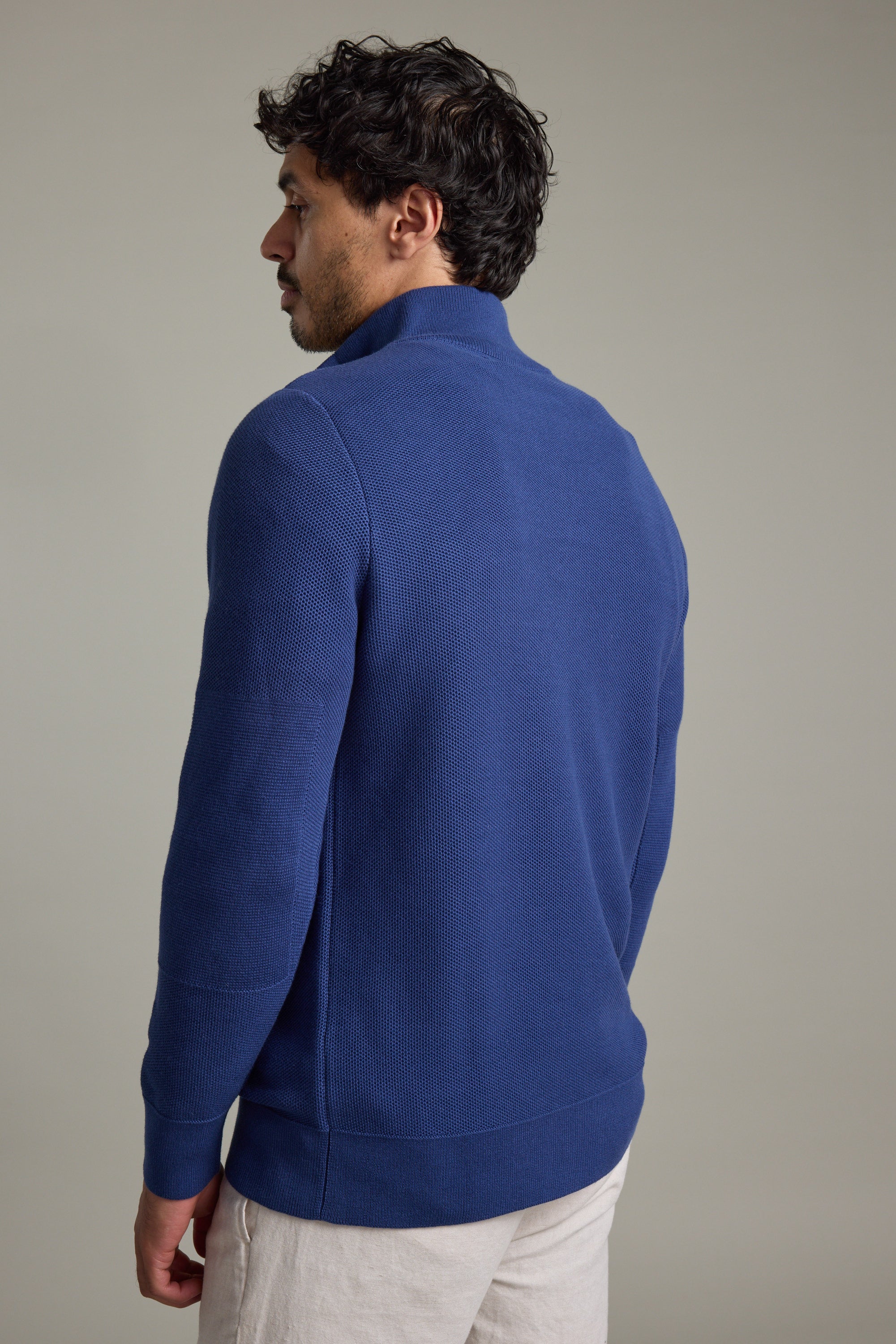 Man in blue Gaston Cotton 1/4 Zip Sweater by Barkers faces away against plain background.