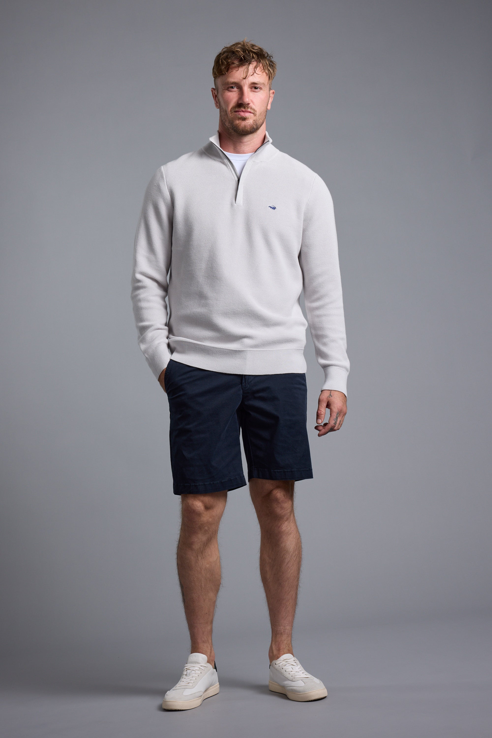 Man wearing the Barkers Gaston Cotton 1/4 Zip Sweater and navy shorts, on a gray background.