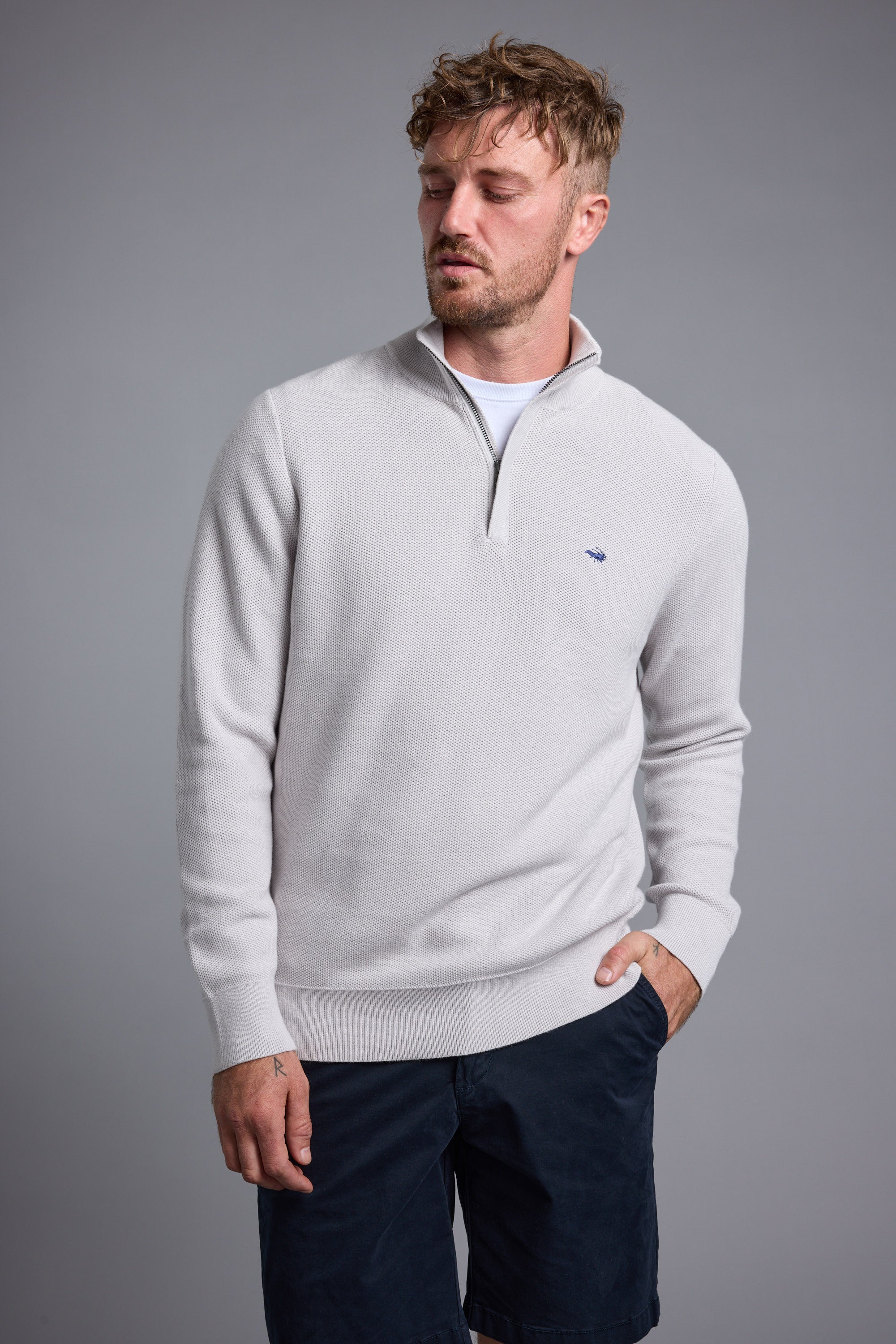 Man in a Barkers Gaston Cotton 1/4 Zip Sweater and navy shorts against a gray background.
