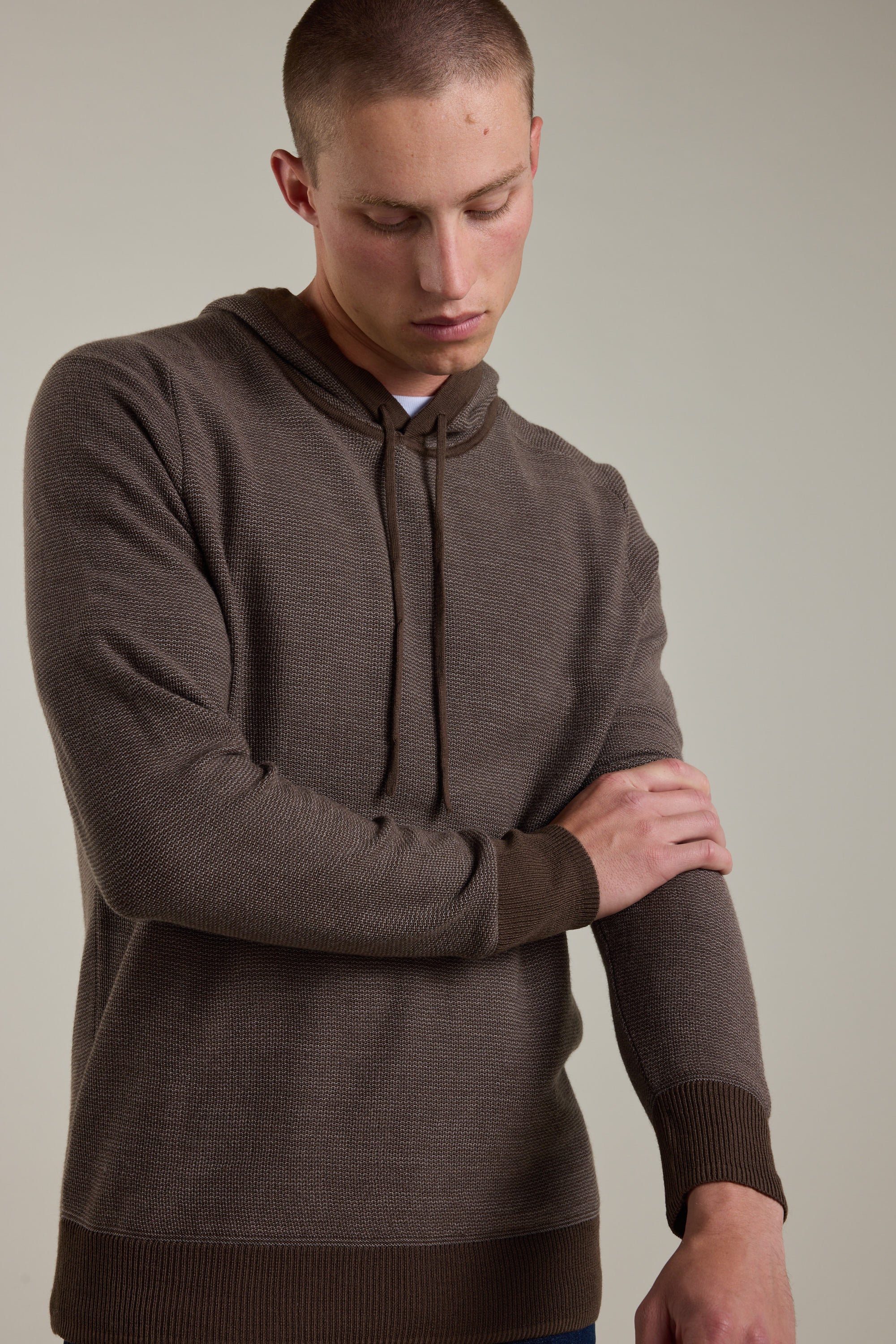 A person in a Barkers Roxbury Merino Hoody with ribbed cuffs and hem looks down, touching their left forearm, set against a plain light background.