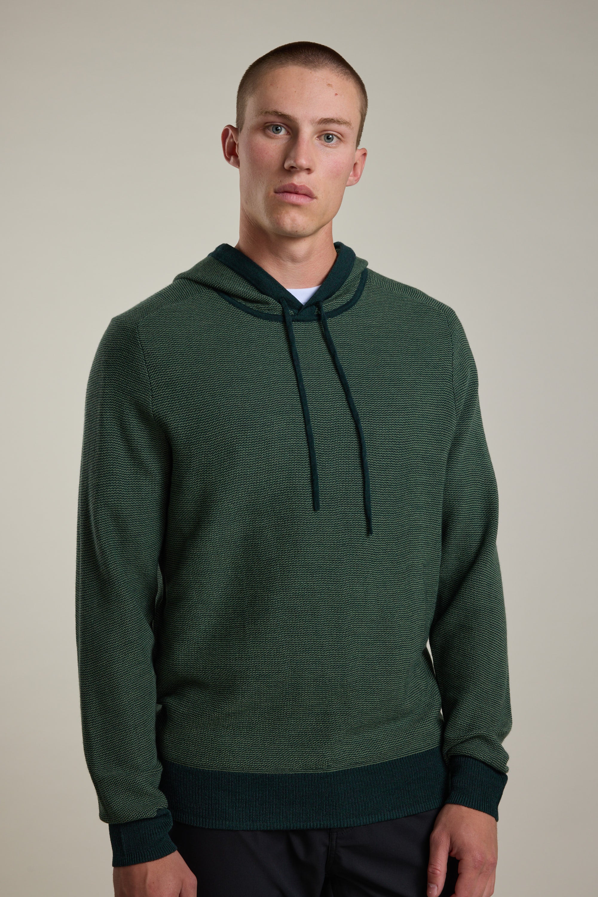 A young man with short hair wears the Barkers Roxbury Merino Hoody, featuring a front pocket and drawstrings, standing against a plain light background and looking directly at the camera with a neutral expression.