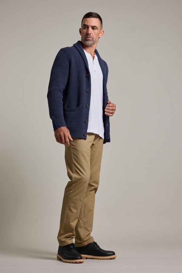 A man in the Barkers Brighton Cotton Shawl Cardi in blue is styled over a white shirt with khaki pants and black shoes. He has short hair, a trimmed beard, and gazes slightly to the side against a plain background.