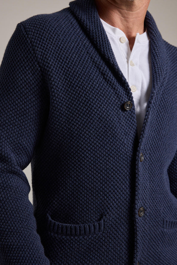 A person wears the Barkers Brighton Cotton Shawl Cardi in textured navy over a white button-up, two buttons fastened and hands in pockets—an ideal winter layering piece.