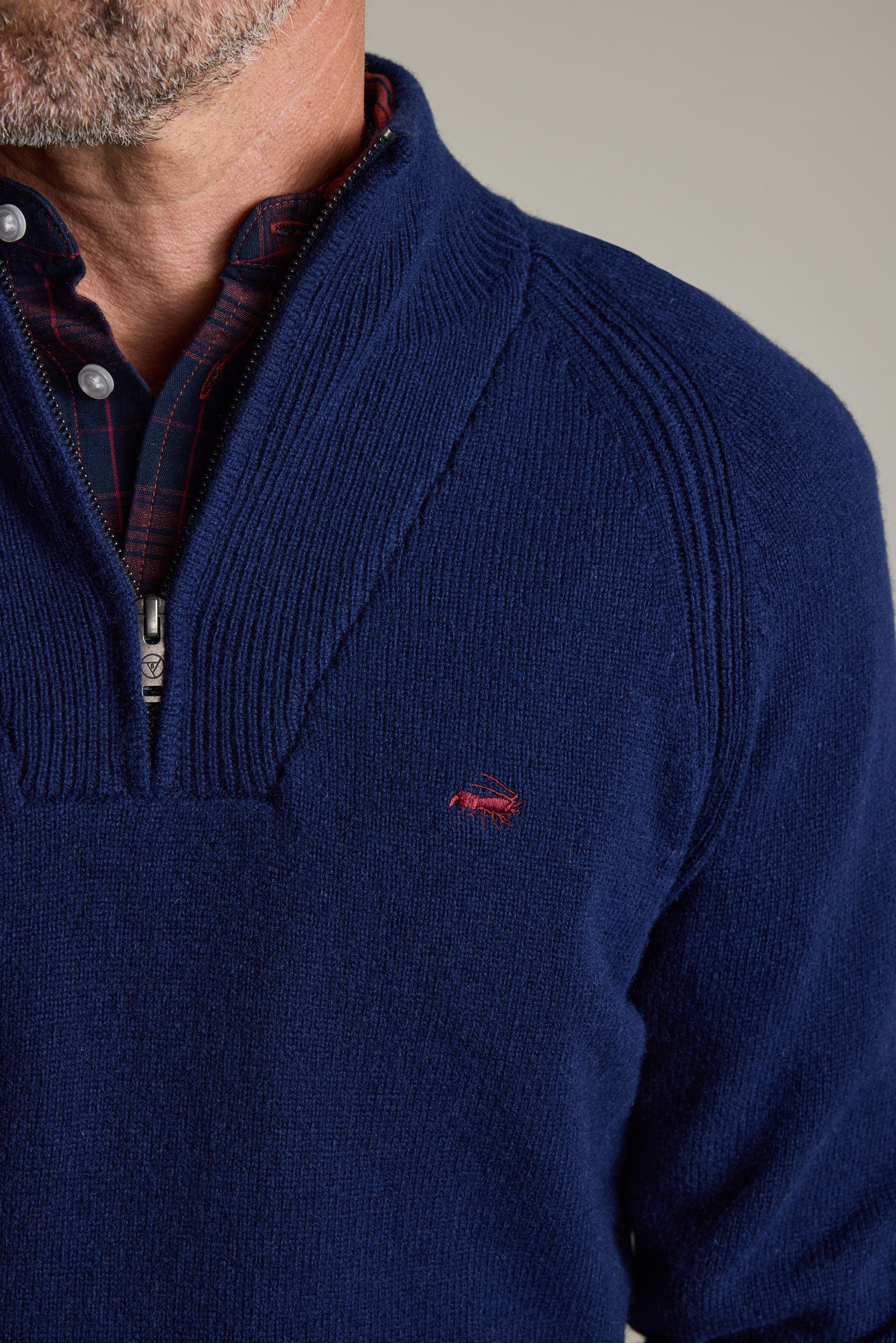 Man in Barkers Rowley Woollen 1/4 Zip navy sweater, over plaid shirt, red chest logo.