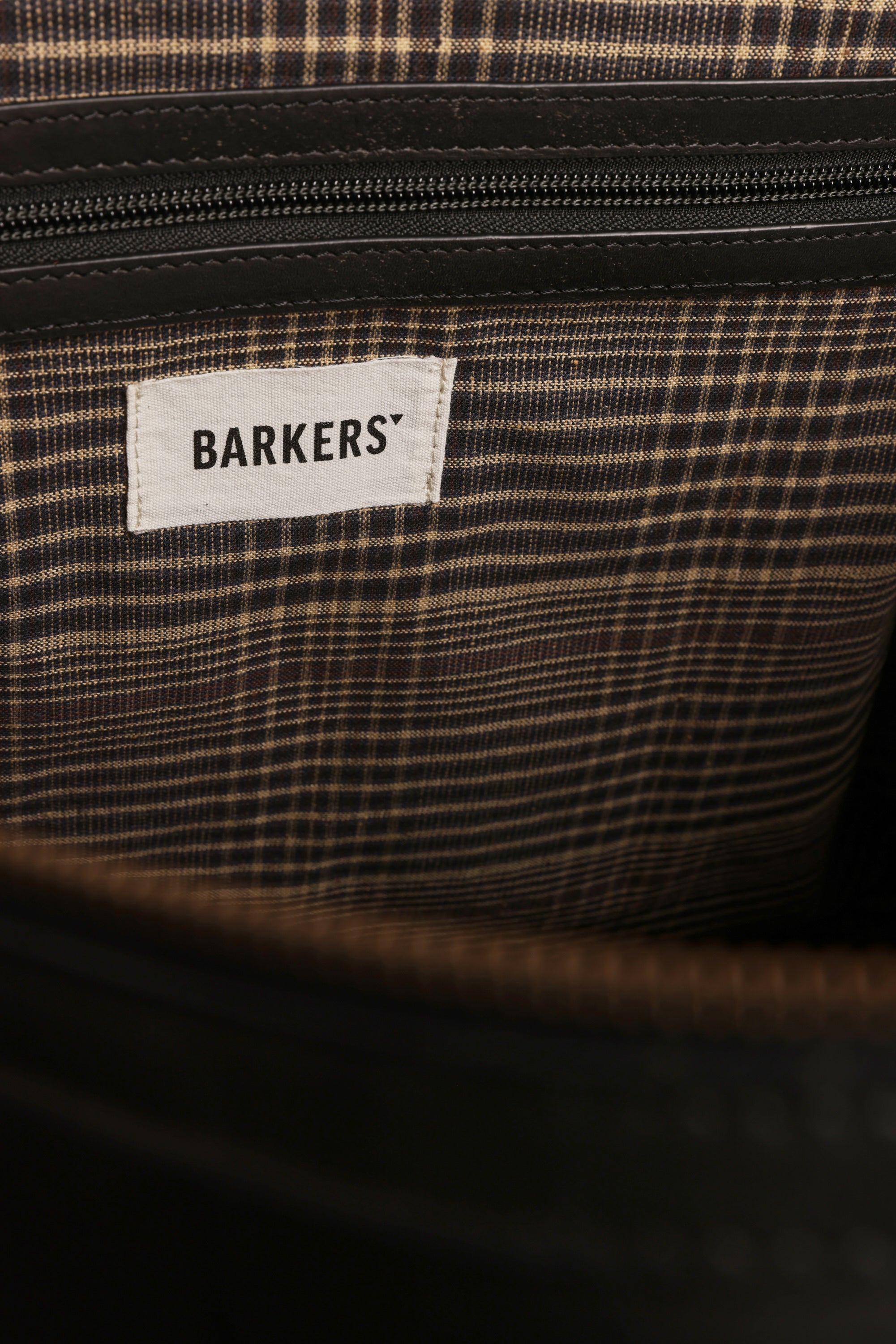 A close-up of the Costello Leather Weekender by Barkers shows its brown plaid fabric lining, a zippered pocket, and a white label marked "BARKERS.