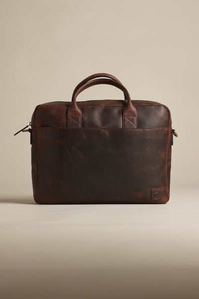 The Barkers Wilkinson Leather Laptop Bag, in dark brown quality leather, features two handles, a zippered top, and a subtle embossed logo in the lower corner, shown against a plain beige background.