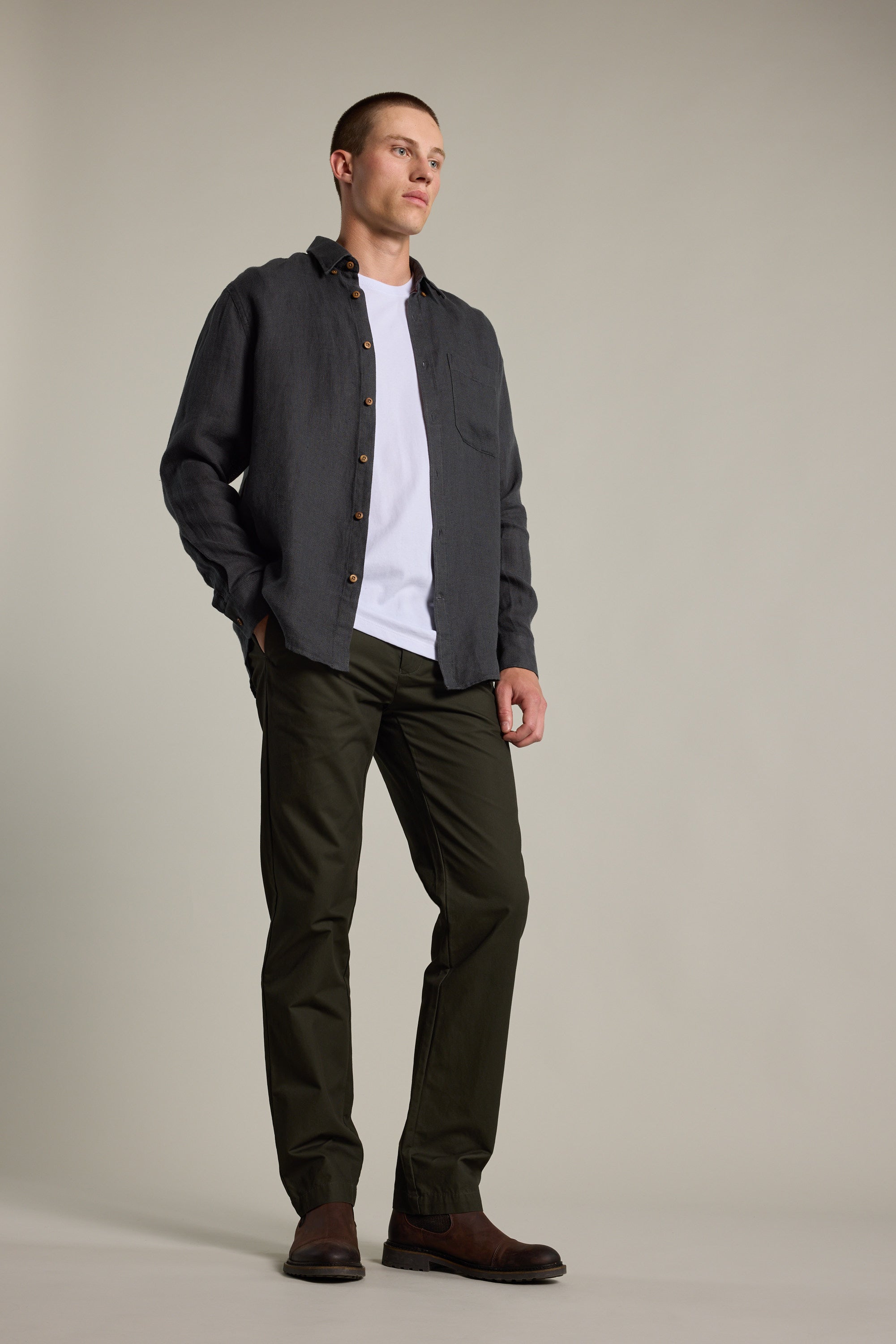 A man stands in a relaxed pose wearing the Barkers Delano Linen Shirt over a white T-shirt, paired with dark pants and brown shoes, set against a plain light background.