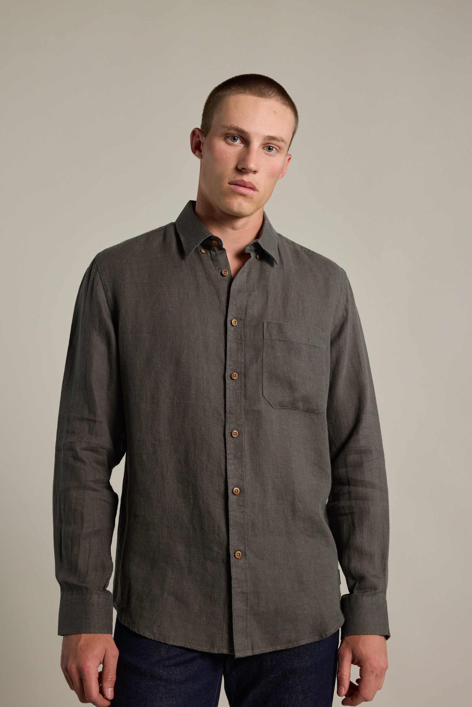 A man with short hair wears the Barkers Delano Linen Shirt in dark grey and dark blue jeans, standing against a light background. He faces the camera with a neutral expression.