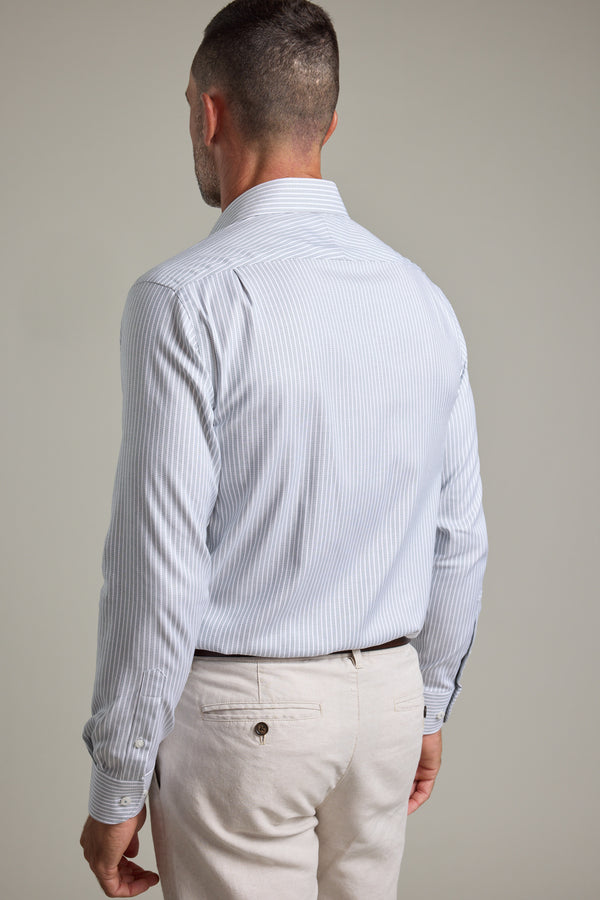 A man stands with his back to the camera, wearing the Barkers Clarke Stripe Business Shirt in light blue and white stripes, paired with light beige pants against a plain background.