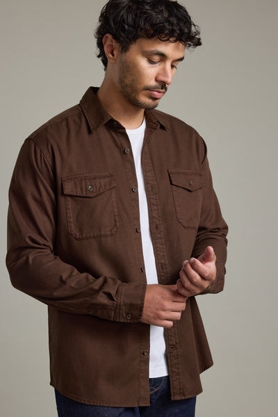 Man in Barkers Darden Shirt adjusts his sleeve while looking down against a gray background.
