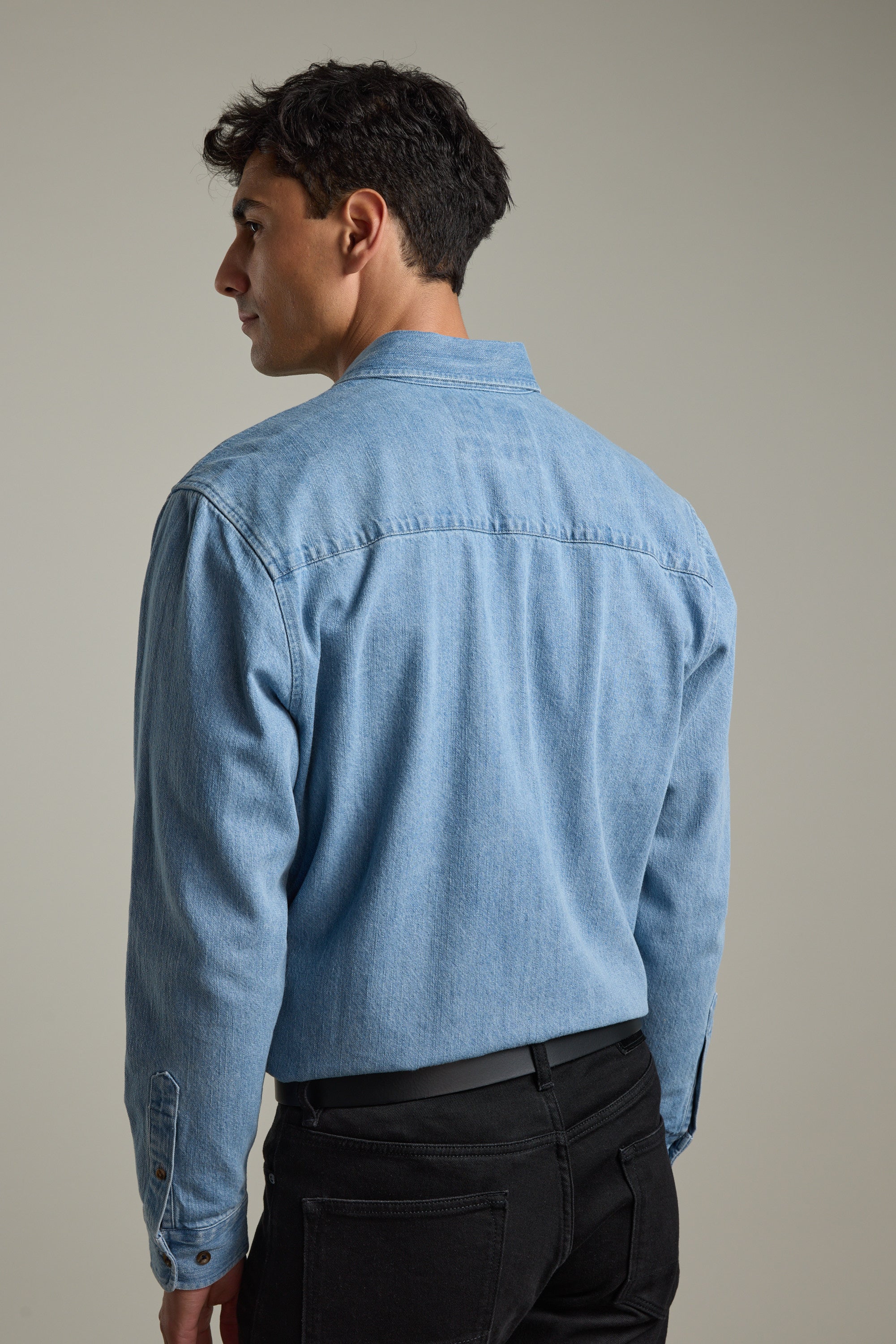 Man in a Barkers Avalon Denim Shirt and black pants standing with his back to the camera.