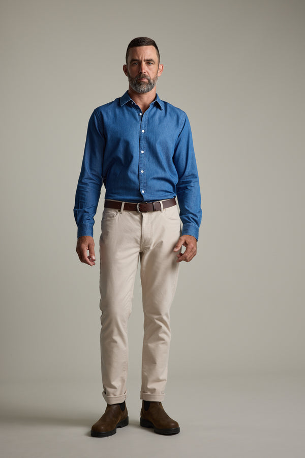 Man in a Wyatt Denim Business Shirt by Barkers, beige pants, and brown boots stands against a plain background.