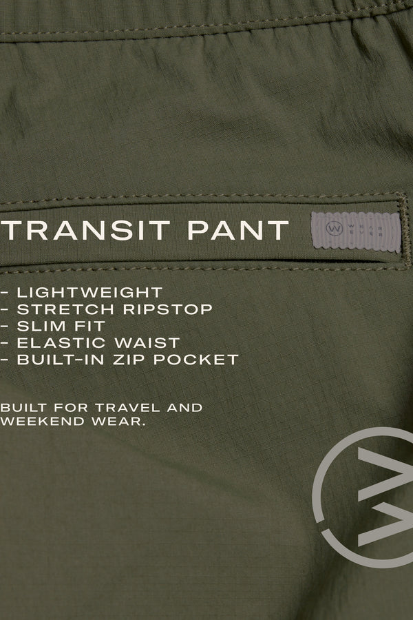 Close-up of olive-green WearEver Transit Pant shows lightweight stretch ripstop fabric, slim fit, elastic waist, and built-in zip pocket. "WearEver Transit Pant" appears with circular logo; fabric texture and stitching are highlighted.