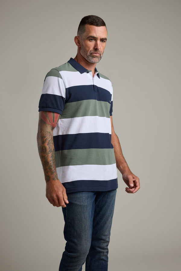 Man in Barkers Regent Pique Stripe Polo and jeans against a plain gray background.