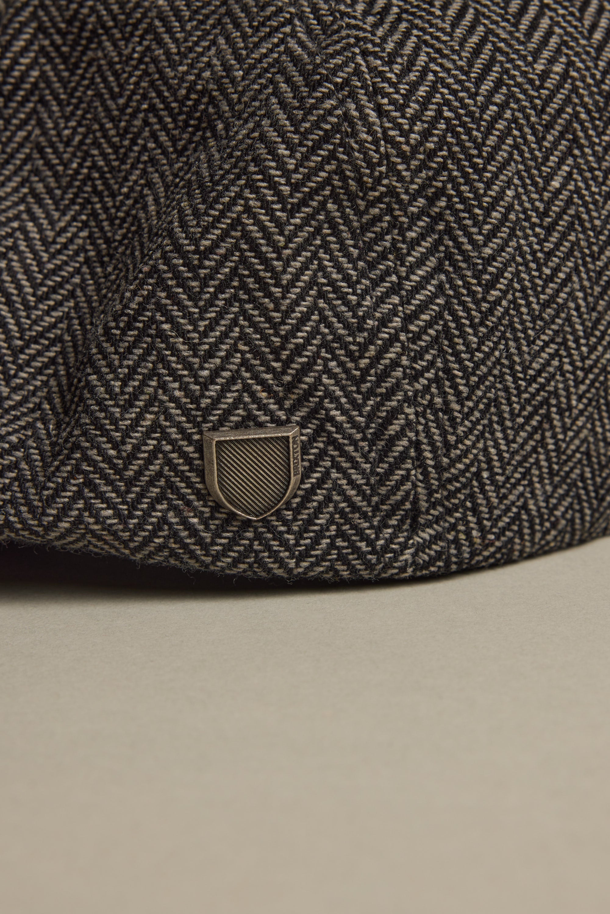 A close-up of the Brixton Brood Snap Cap in herringbone wool with a small metallic emblem.