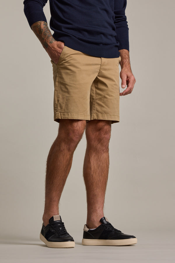 A person wearing Barkers' Kingly Chino Short, navy long-sleeve shirt, and black sneakers stands with one hand in their pocket. Only their lower half is visible against a plain background.