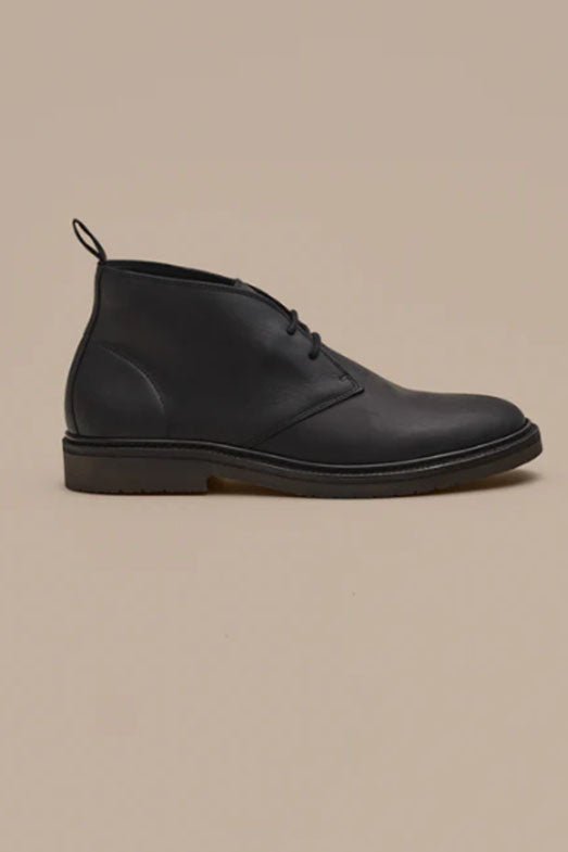 The Barkers Howarth Desert Boot, a black leather lace-up ankle boot with low heel and round toe, is showcased in profile on a beige background, reflecting the quality of Portuguese footwear craftsmanship.