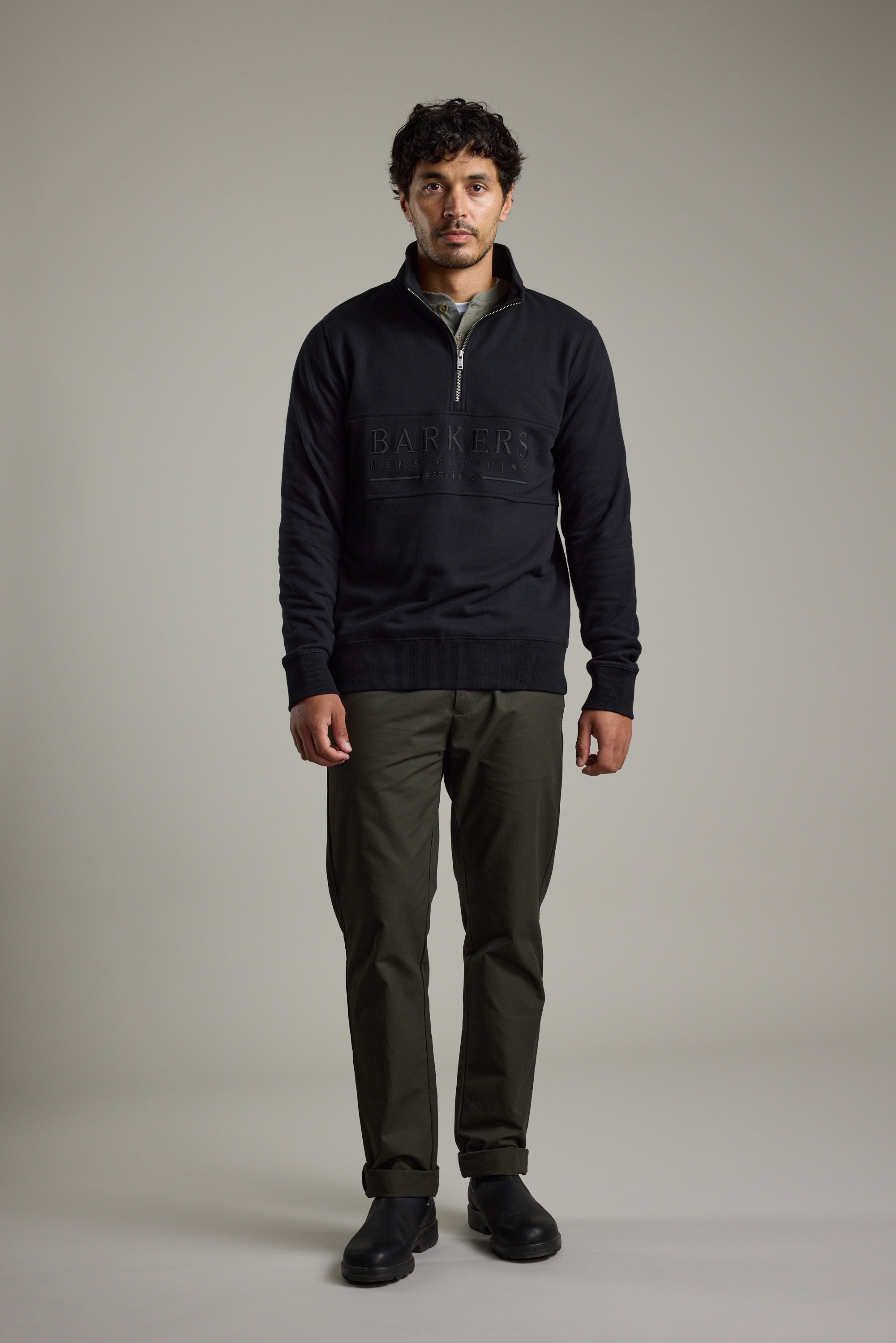 Man in studio wearing Barkers Heritage 1/4 Zip sweatshirt, olive pants, and black shoes.