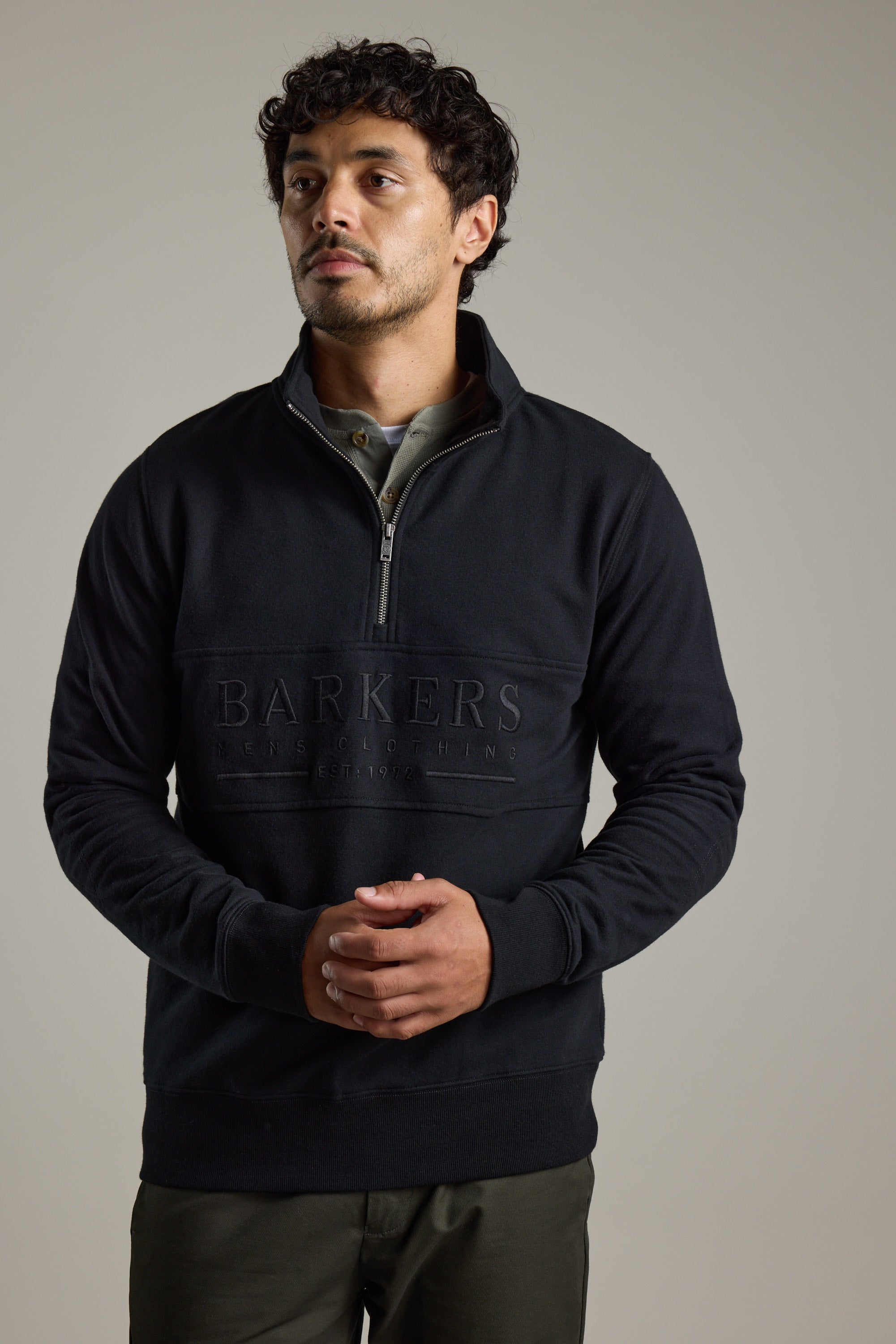 Man in Barkers Heritage 1/4 Zip sweater and olive pants, standing with hands clasped.