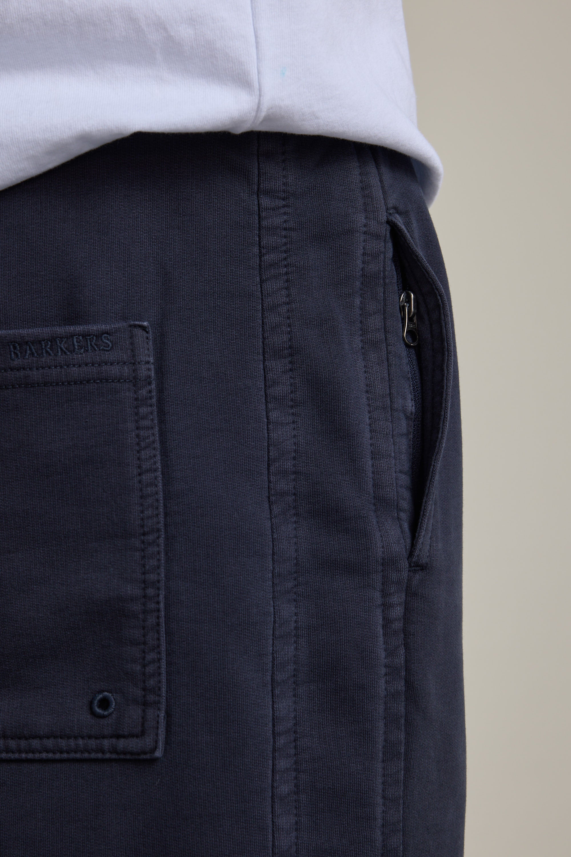 Close-up of a person wearing Barkers Organic Classic Print Track Pant in navy, featuring a back pocket, visible stitching, and the Barkers brand label above the pocket—evoking a classic '90s trackies vibe. Paired with a white shirt.