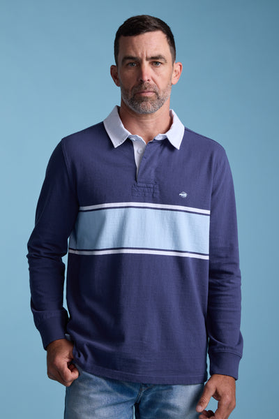 A man with short dark hair and a trimmed beard wears the Barkers Breaker Rugby Jersey—navy blue with light blue and white stripes, a white collar, and made from organic cotton—standing against a plain blue background.
