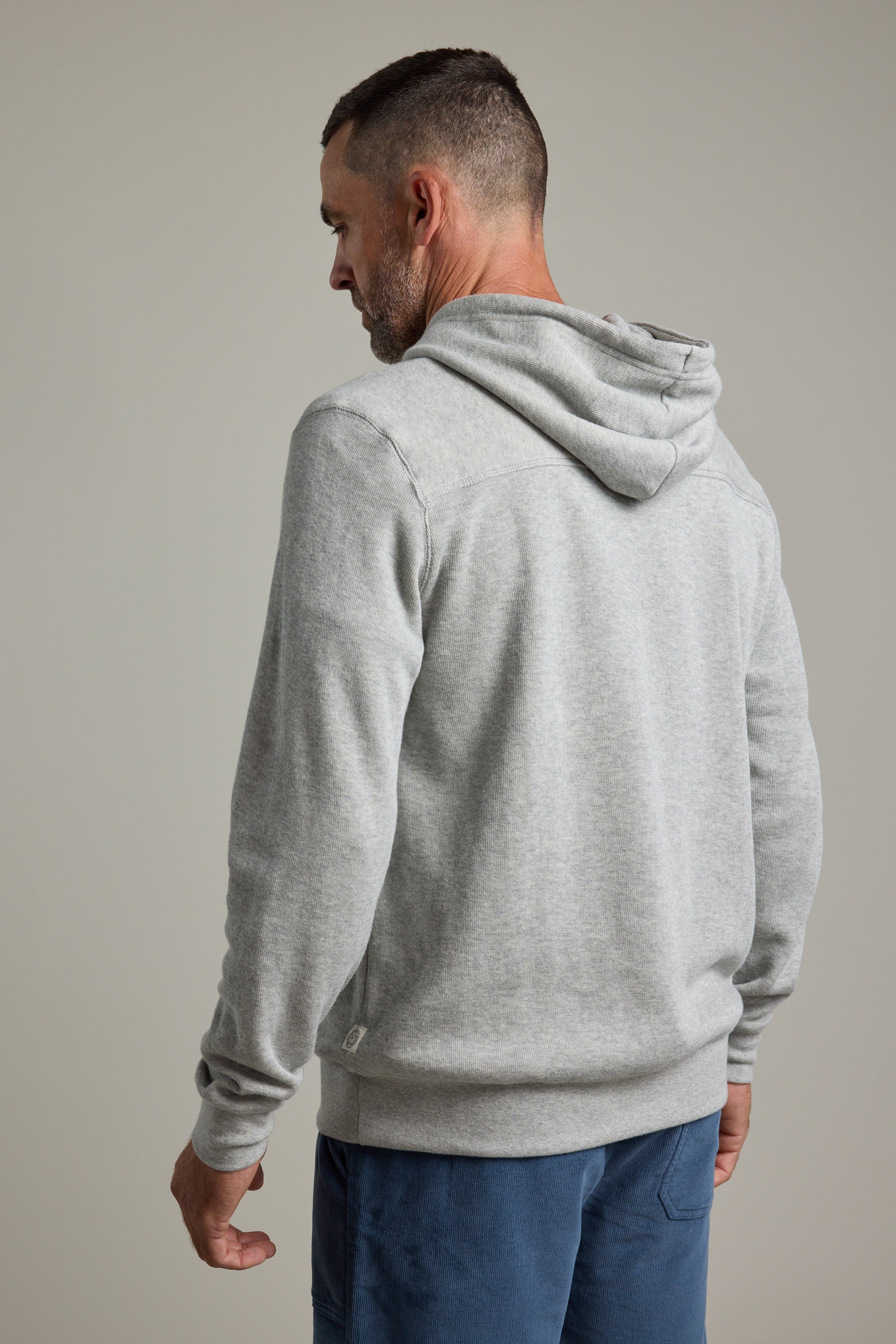 A man with short hair and a beard, facing away from the camera, wears the Barkers Inlet Hoody in light gray and blue pants against a plain background.