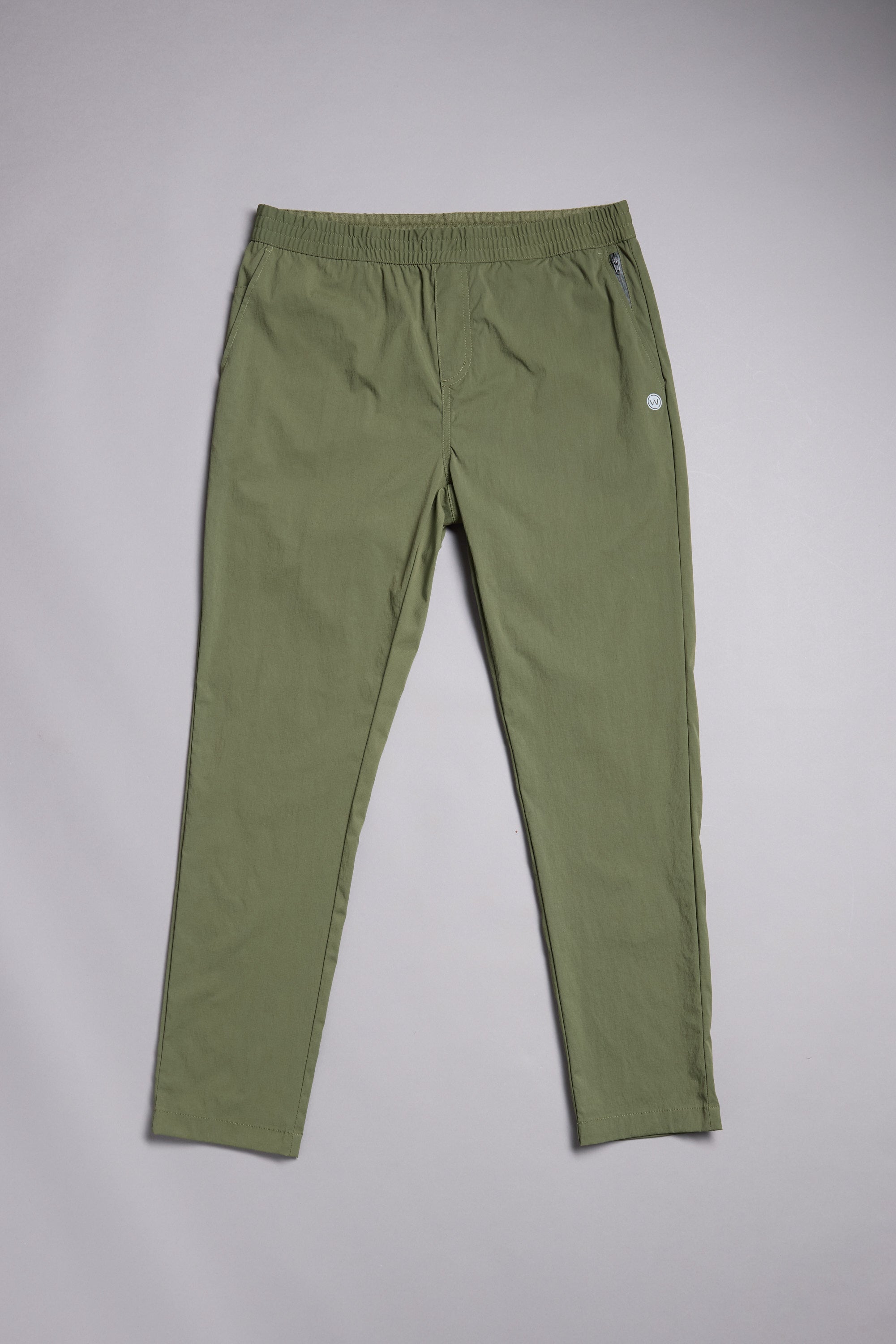 The WearEver Transit Pant by WearEver, in olive green, features a slim fit, elastic waistband, and buttoned side pocket; shown laid flat on a plain light gray background.