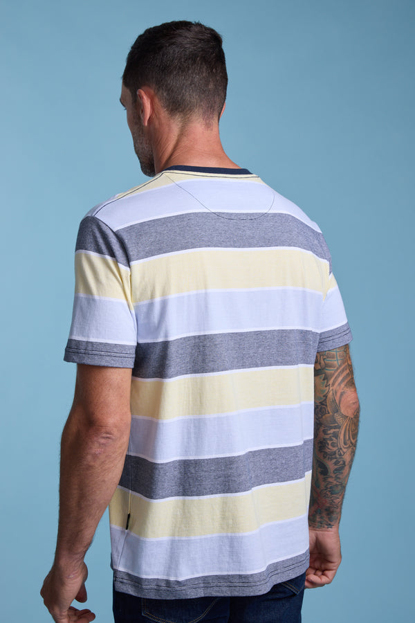 A man with short dark hair, seen from behind, wears the Barkers Asbrooke Stripe Tee in white, gray, and light yellow. He has a sleeve tattoo on his left arm and stands against a light blue background.