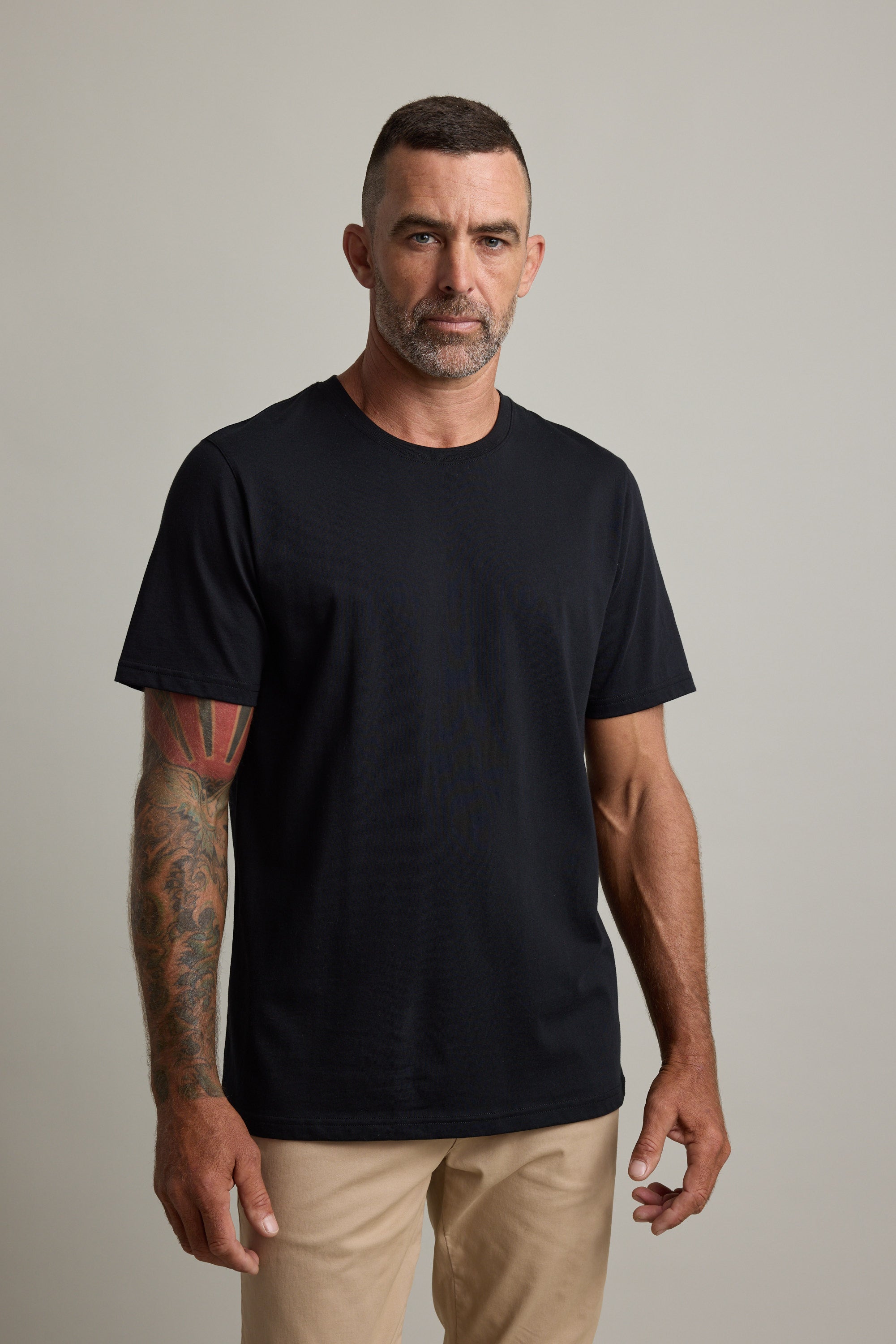 Man with tattoos wearing a Barkers Good Earth Cotton Essential Tee and beige pants.