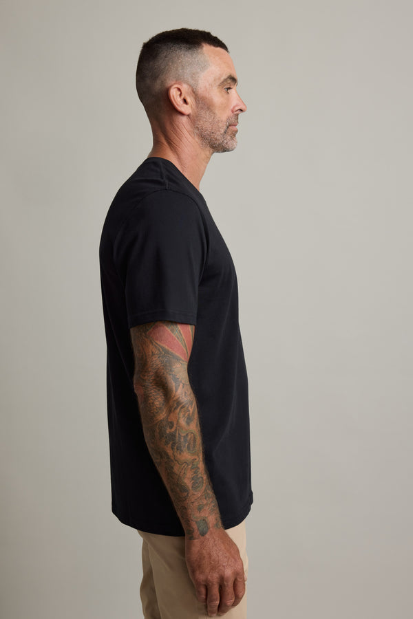 Man in a Barkers Good Earth Cotton Essential Tee and beige pants, showing arm tattoos in profile.