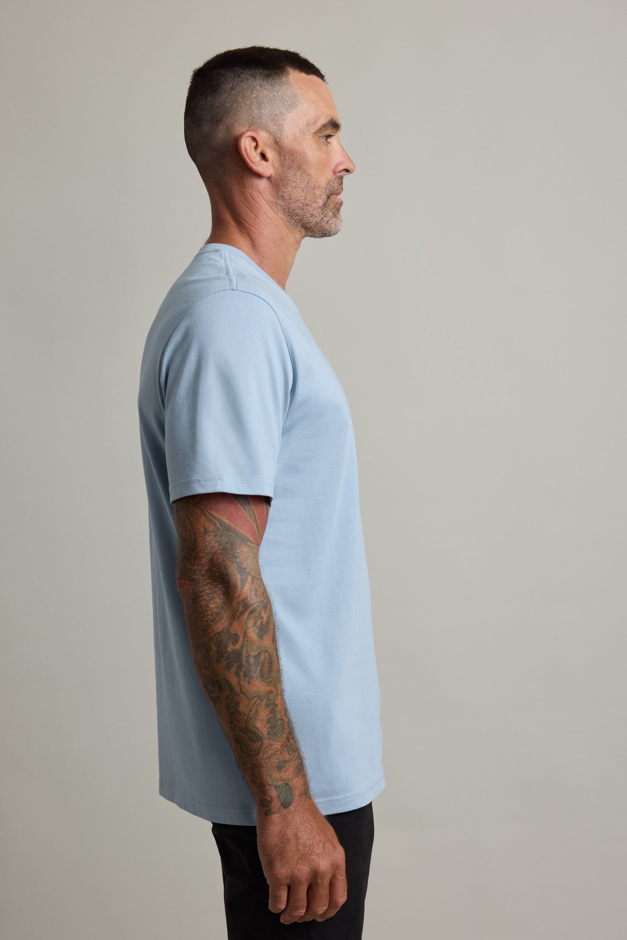 Man with tattoos in a Barkers Good Earth Cotton Essential Tee, profile view against plain background.