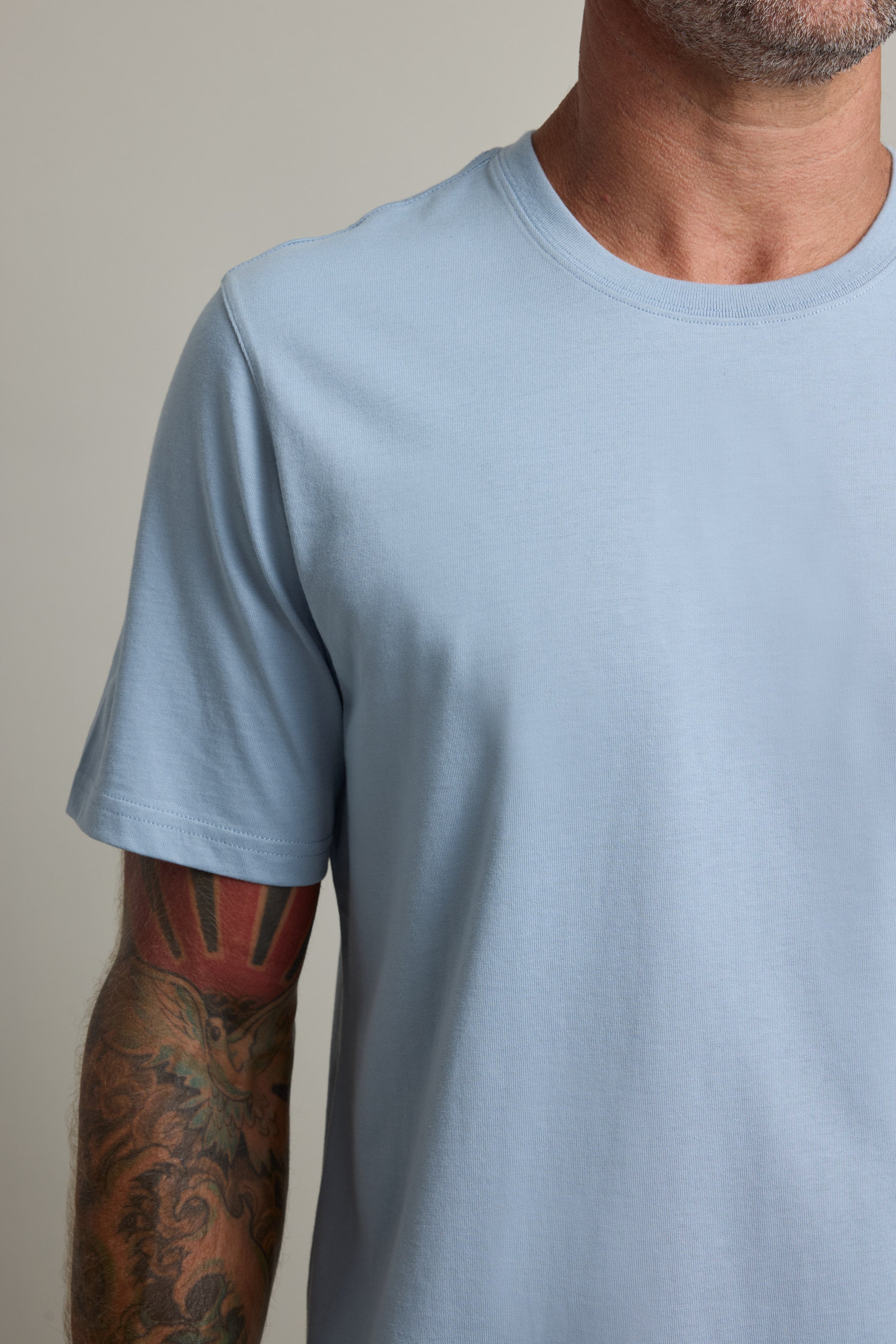 A man in a Good Earth Cotton Essential Tee by Barkers with a colorful tattoo on his left forearm.