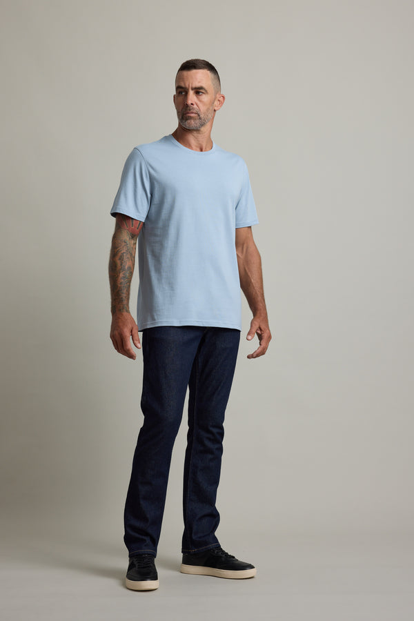 Man in a light blue Barkers Good Earth Cotton Essential Tee, dark jeans, and black sneakers.