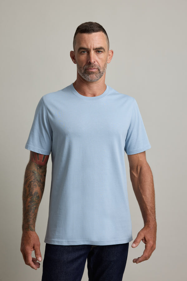 Man with short hair and tattoos in a Barkers Good Earth Cotton Essential Tee and dark jeans, facing forward.